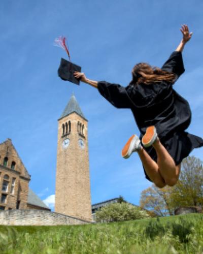Cornell graduate jumping into the air with Uris Clock Tower in the background